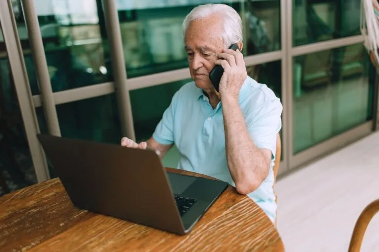 Desaposentação e reaposentacao: o que continua possível para quem volta a trabalhar 2 Elderly man multitasking, using laptop and phone at home. Lifestyle image.