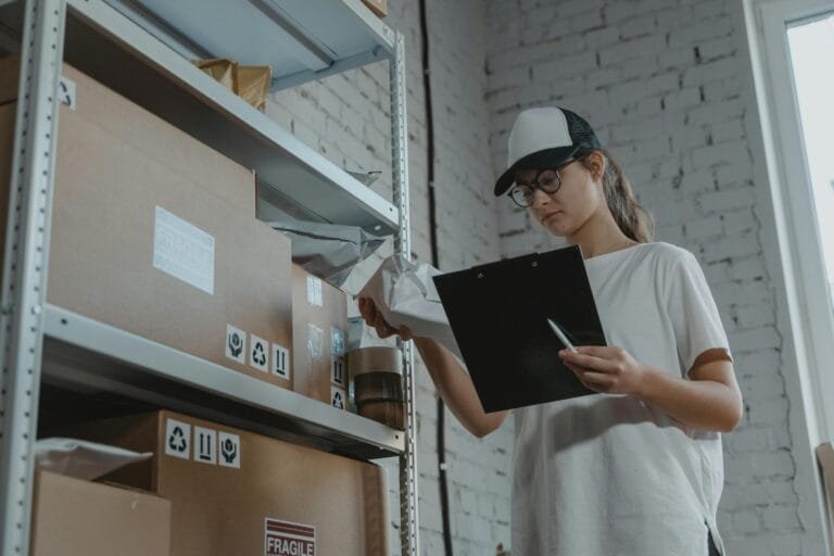 DIFAL do ICMS: Impactos no E-commerce 3 Warehouse worker organizing packages on shelf with clipboard.