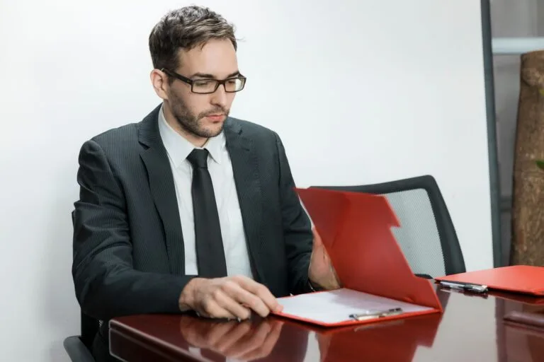 Professional man in suit reviewing papers at office desk with focus and determination.