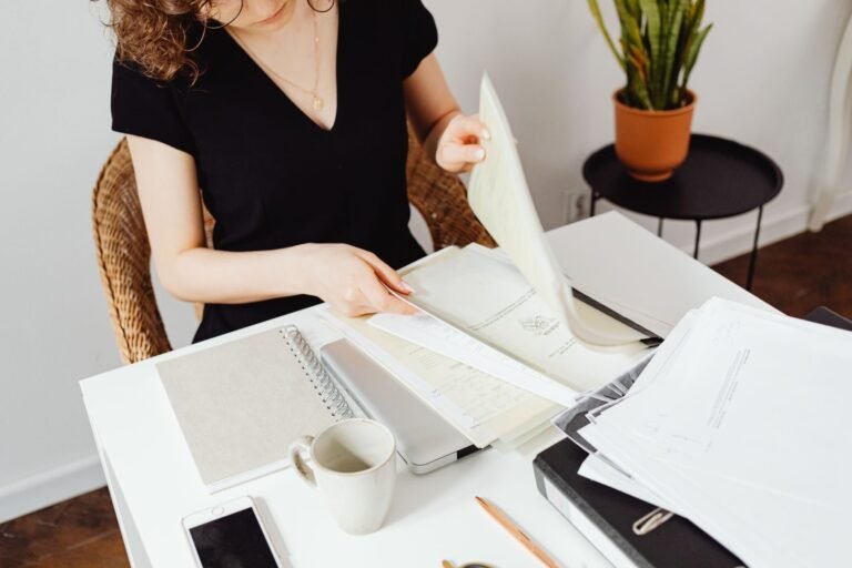 Woman sorting through documents in a home office setting. Organized workspace with plants.