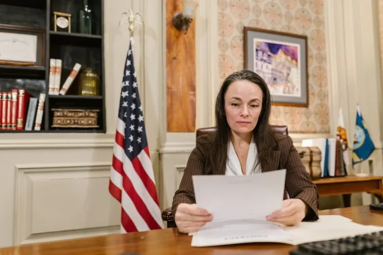A professional woman reviewing legal documents in an office with flags and books.