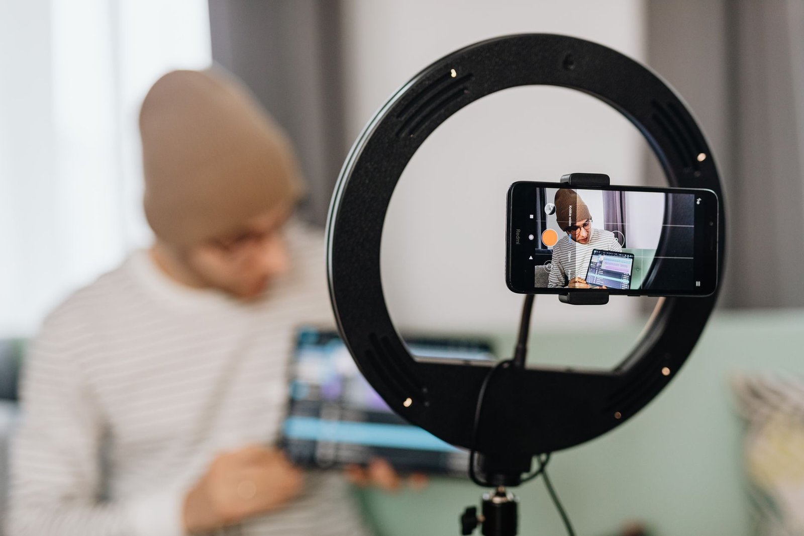 Man vlogging with a smartphone and ring light, focused on content creation indoors.