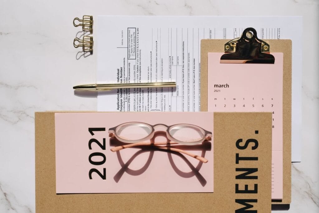 Top view of office supplies including glasses, documents, and clipboard on a marble desk.