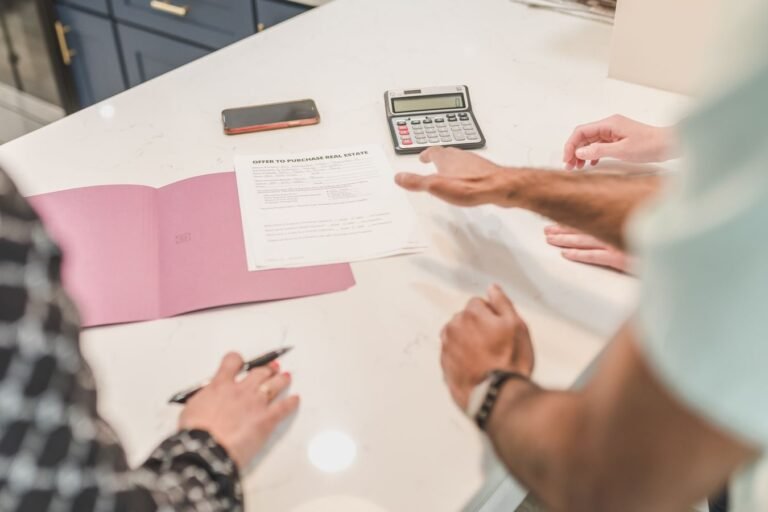 Due diligence na compra de imovel: as certidoes que evitam prejuizo no negocio 7 Hands gesturing during a real estate document review on a modern office desk with a calculator.