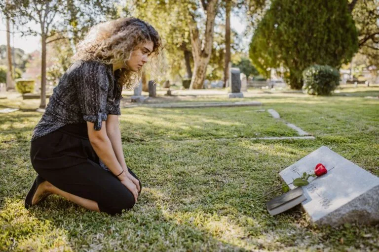 Duração da pensão por morte: as regras de prazo conforme idade e tempo de união 2 A woman kneeling by a grave in a sunlit cemetery, expressing grief and remembrance.