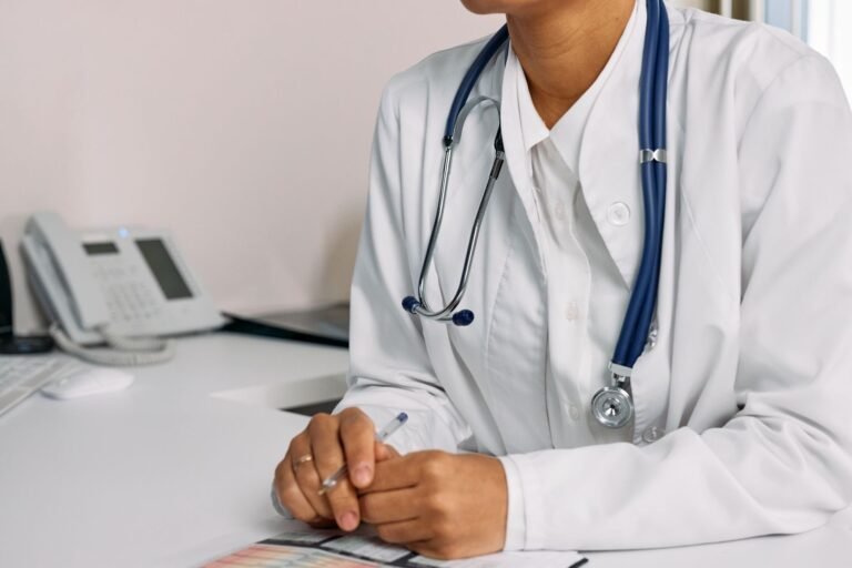 Eliminacao na investigacao social e no exame medico de concurso 2 Doctor with stethoscope and white coat seated at a clinic desk.