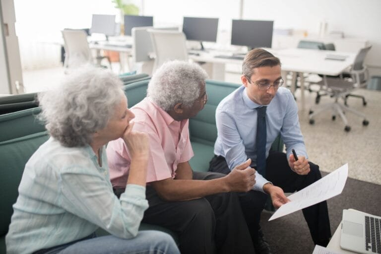 Entrada Aposentadoria Meu INSS 2026: Passo a Passo Completo 4 Business professional consults elderly clients in an office setting. Collaborative discussion, paperwork visible.