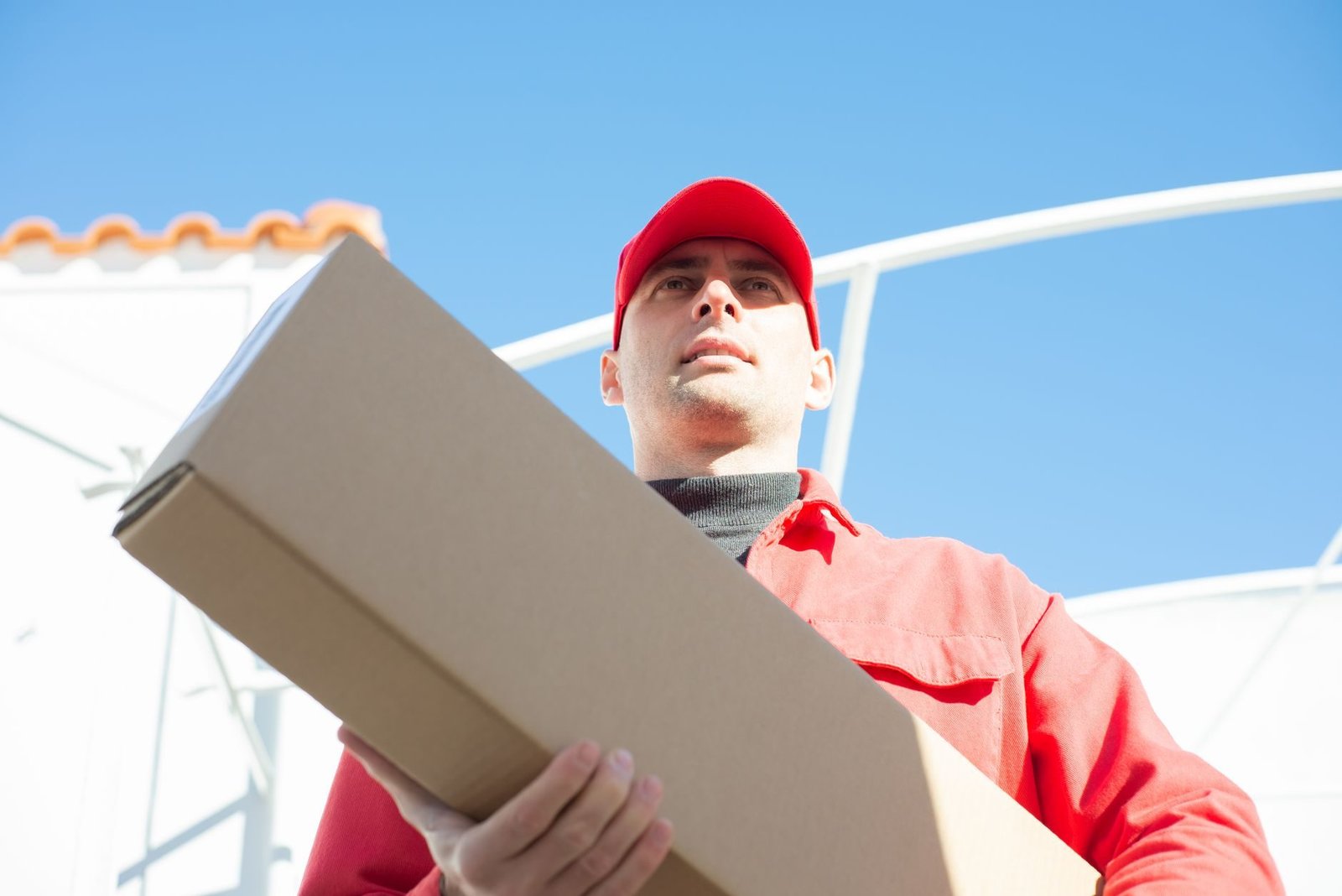 Delivery person in red uniform holding a parcel, captured with a low angle against a clear