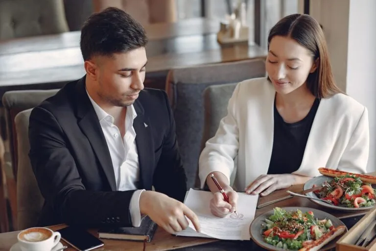 Concentrated multiethnic colleagues in formal clothes sitting at table in cafe with cup of espresso and plates of salad 