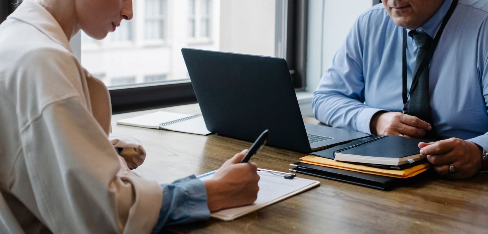 Estabilidade no emprego: as situacoes que protegem o trabalhador da demissao 1 Crop faceless colleagues in formal clothes sitting at table with laptop and folder and signing documents while working t