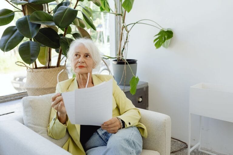 Fator previdenciário: quando ele ainda incide e como reduz ou eleva o beneficio 14 Senior woman in casual setting reviewing documents indoors.