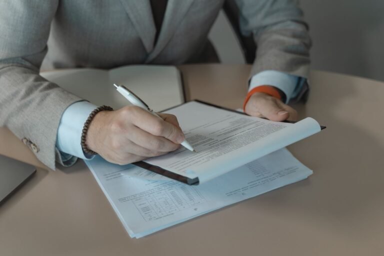 Close-up of business person signing documents at a desk with a pen.