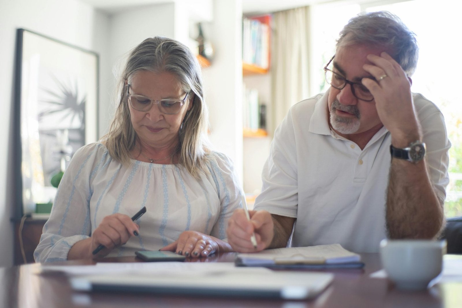 Fibromialgia e INSSAposentadoria por Invalidez é Possível? 1 Senior couple calculating expenses at home office desk with documents and notes.