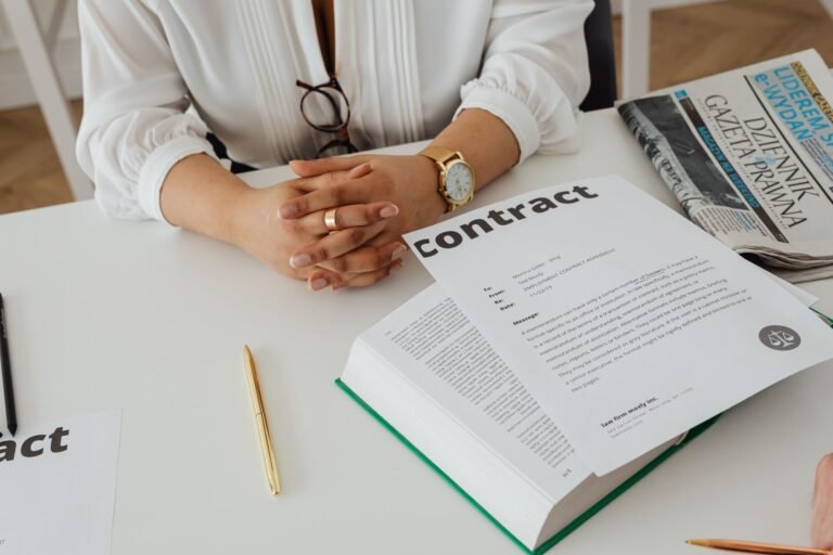 Garantia legal e garantia contratual: o que cobrir quando o produto da defeito 2 Businesswoman sitting at desk reviewing contract with legal documents and newspaper.
