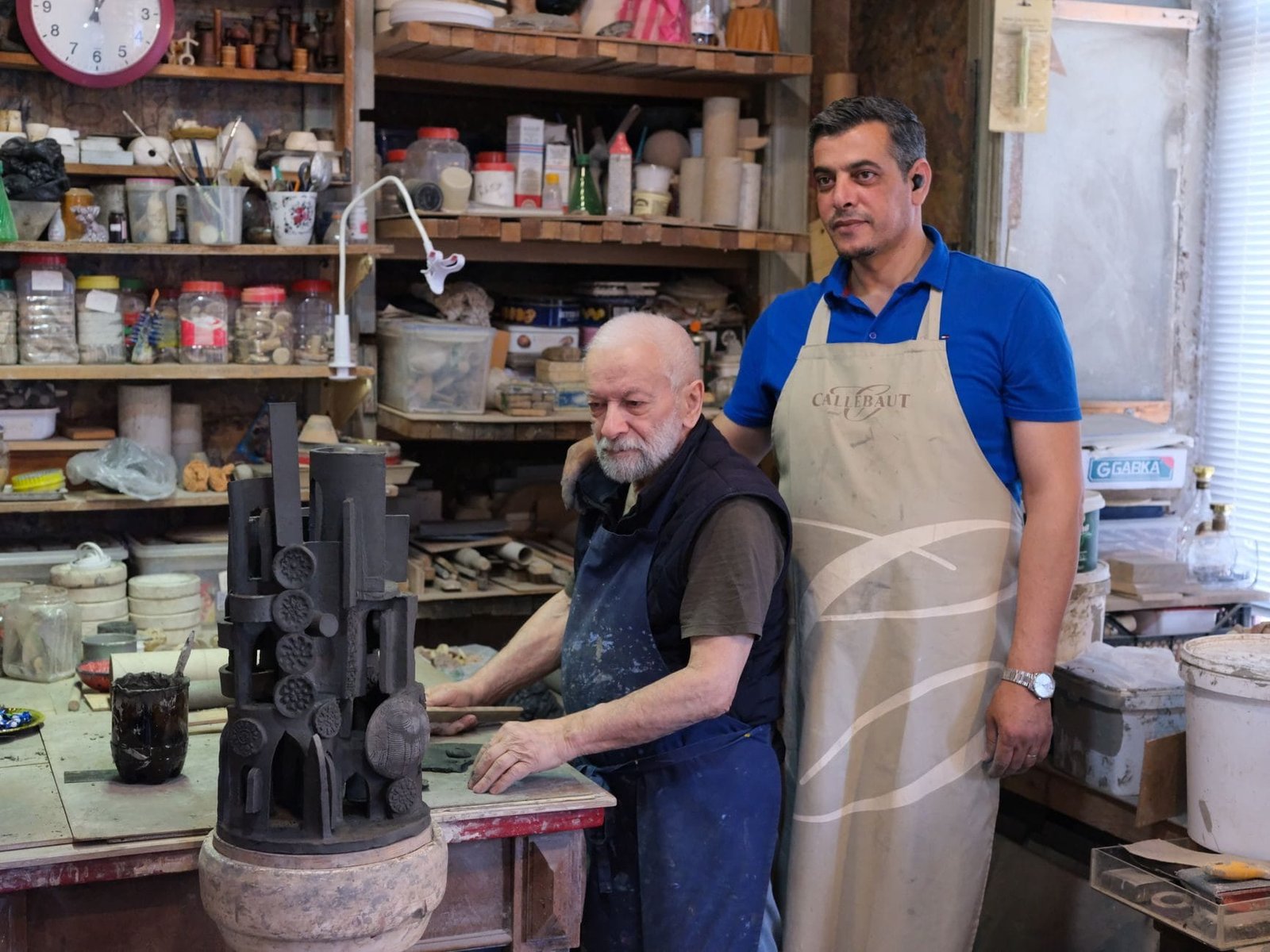 Elderly sculptor and younger apprentice working on pottery in an artisans studi