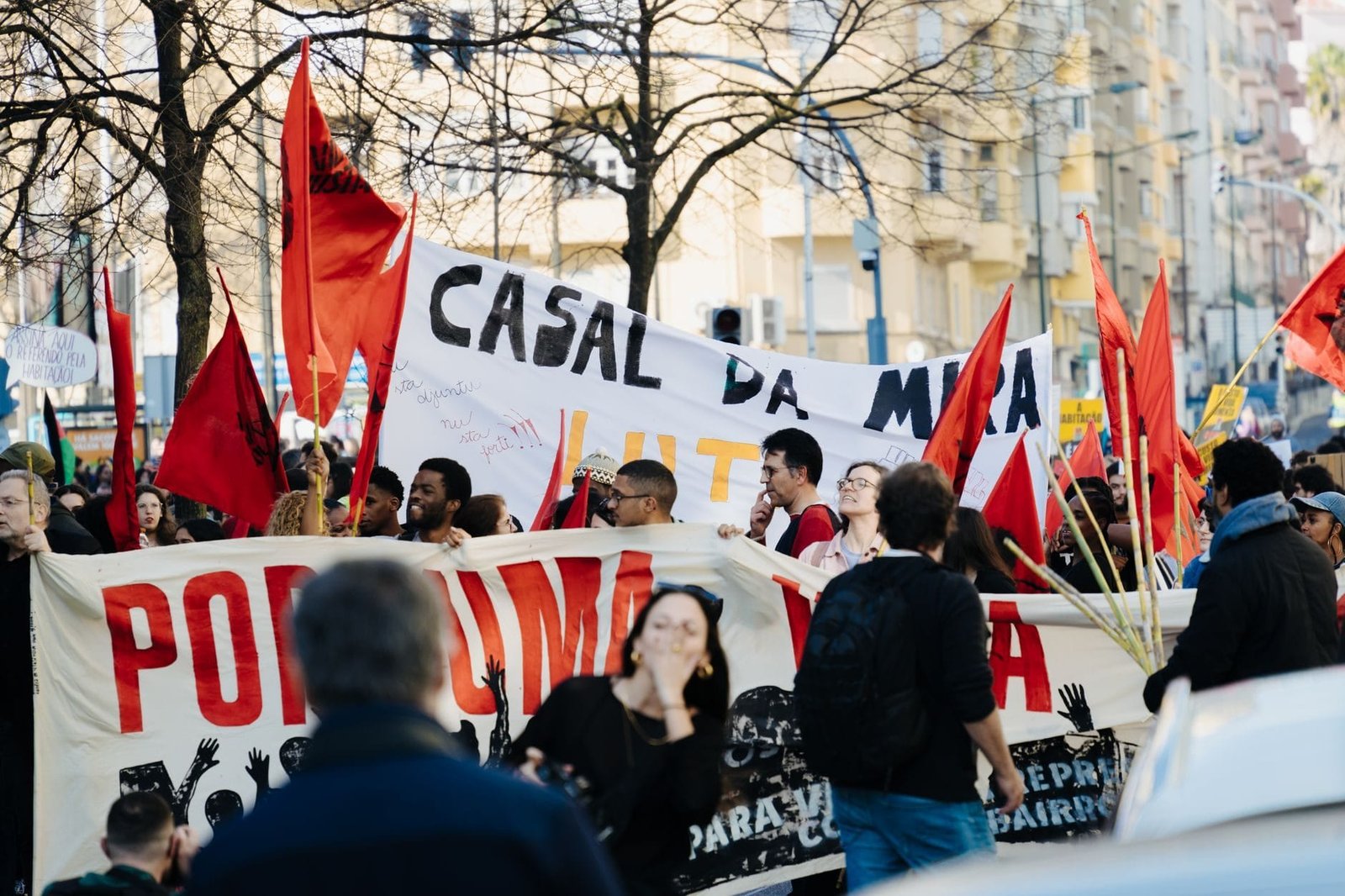 Group of people in a city staging a protest with banners and red flags during th