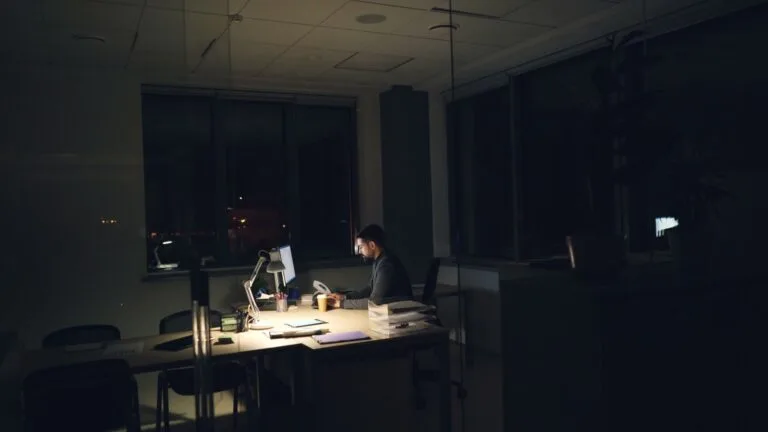 A man working late at night in an office, illuminated by desk light.