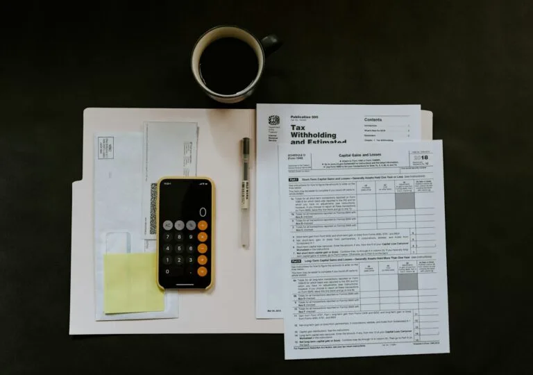 black Android smartphone near ballpoint pen, tax withholding certificate on top of white f