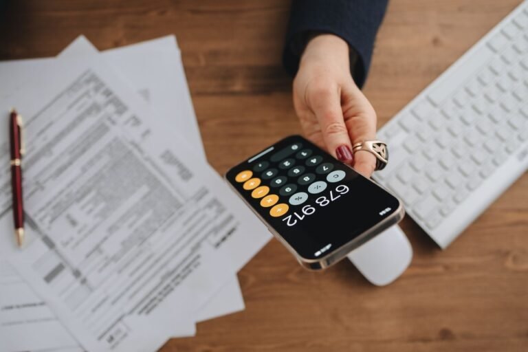 Imposto de Renda da pessoa fisica: deducoes, malha fina e como se defender 6 Hand holding smartphone calculator over tax documents on desk.