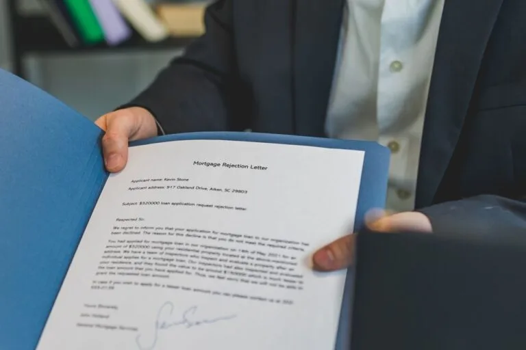 Close-up view of a person holding a mortgage rejection letter in a folder, indoors.