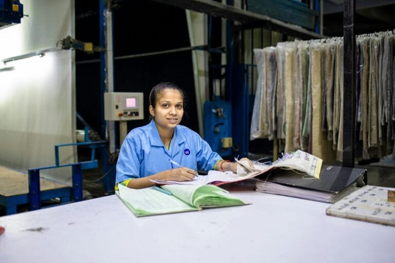 Female textile worker in factory reviewing documents at a desk.
