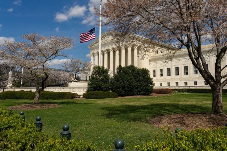 A view of a neoclassical government building with an American flag and cherry blossoms in 