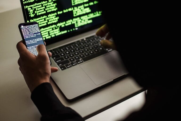 Invasão de dispositivo e conta hackeada: o crime, a prova e os primeiros movimentos 13 From behind crop male programmer in black hood browsing netbook and mobile phone while wor
