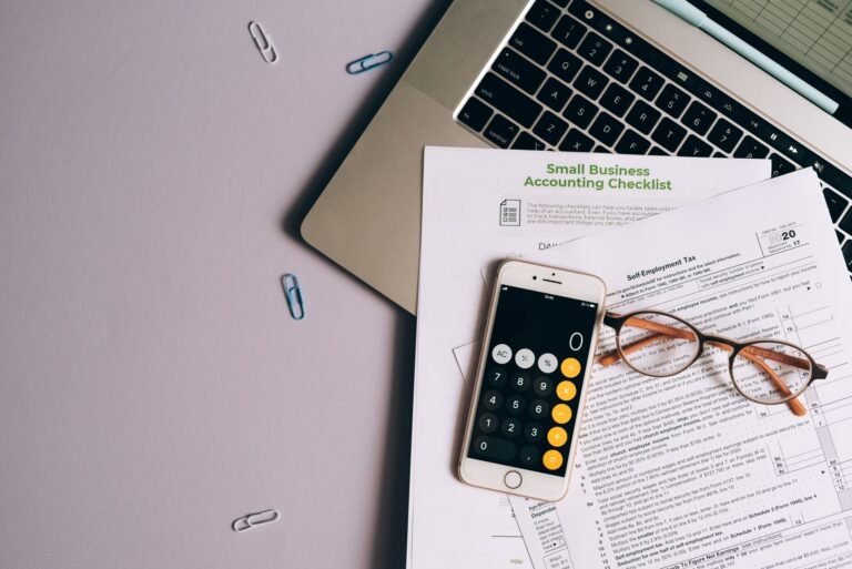 Flat lay of small business accounting tools including tax form, phone, and glasses on a de
