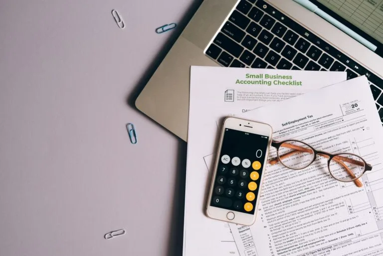 IPVA: incidência, isenções e como contestar cobranças indevidas 2 Flat lay of small business accounting tools including tax form, phone, and glasses on a de