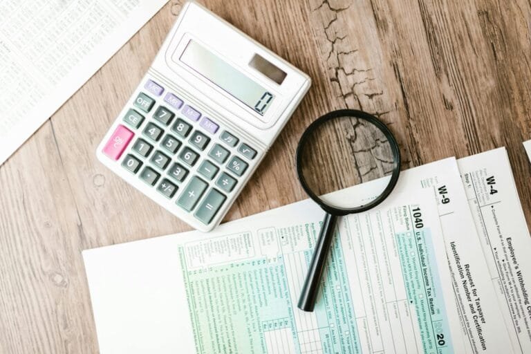 IRPF sobre Ganho de Capital na Venda de Imóvel 3 Tax forms laid out with a calculator and magnifying glass on a wooden surface, perfect for finance themes.