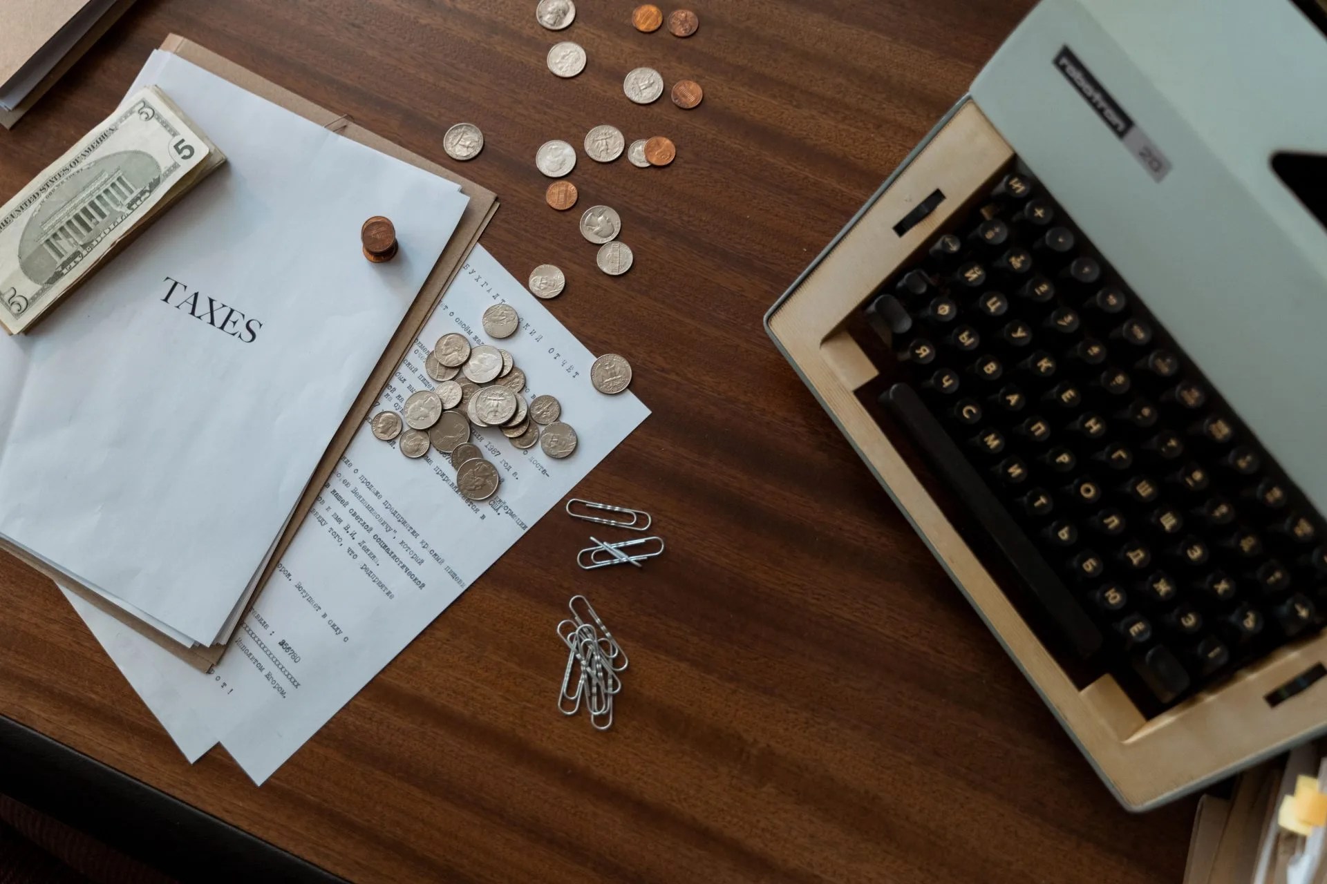 Overhead view of a vintage desk with typewriter, coins, and tax documents.