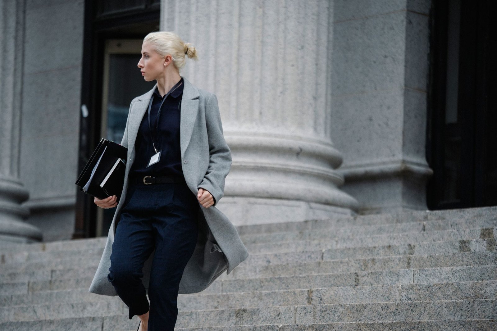 Serious female lawyer in elegant outfit holding folders with documents while going downsta