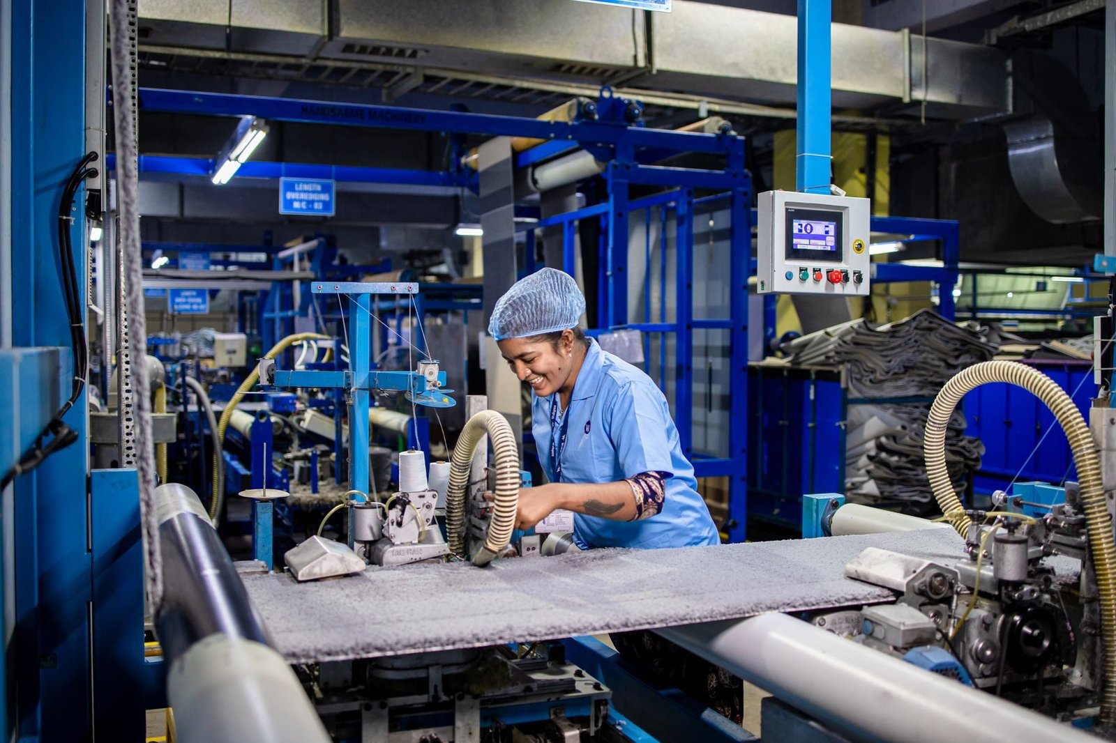Indian female factory worker smiling while operating complex textile machinery in an indus