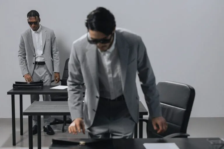 Lesão corporal em briga: consequências criminais e civis 7 Two businessmen in grey suits and sunglasses in a modern office setting with briefcases.