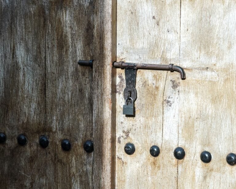 Close-up of a weathered wooden door with a vintage iron padlock in sunlight.