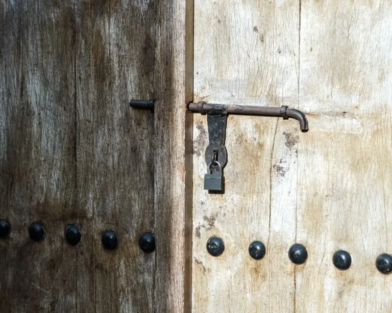 Close-up of a weathered wooden door with a vintage iron padlock in sunlight.