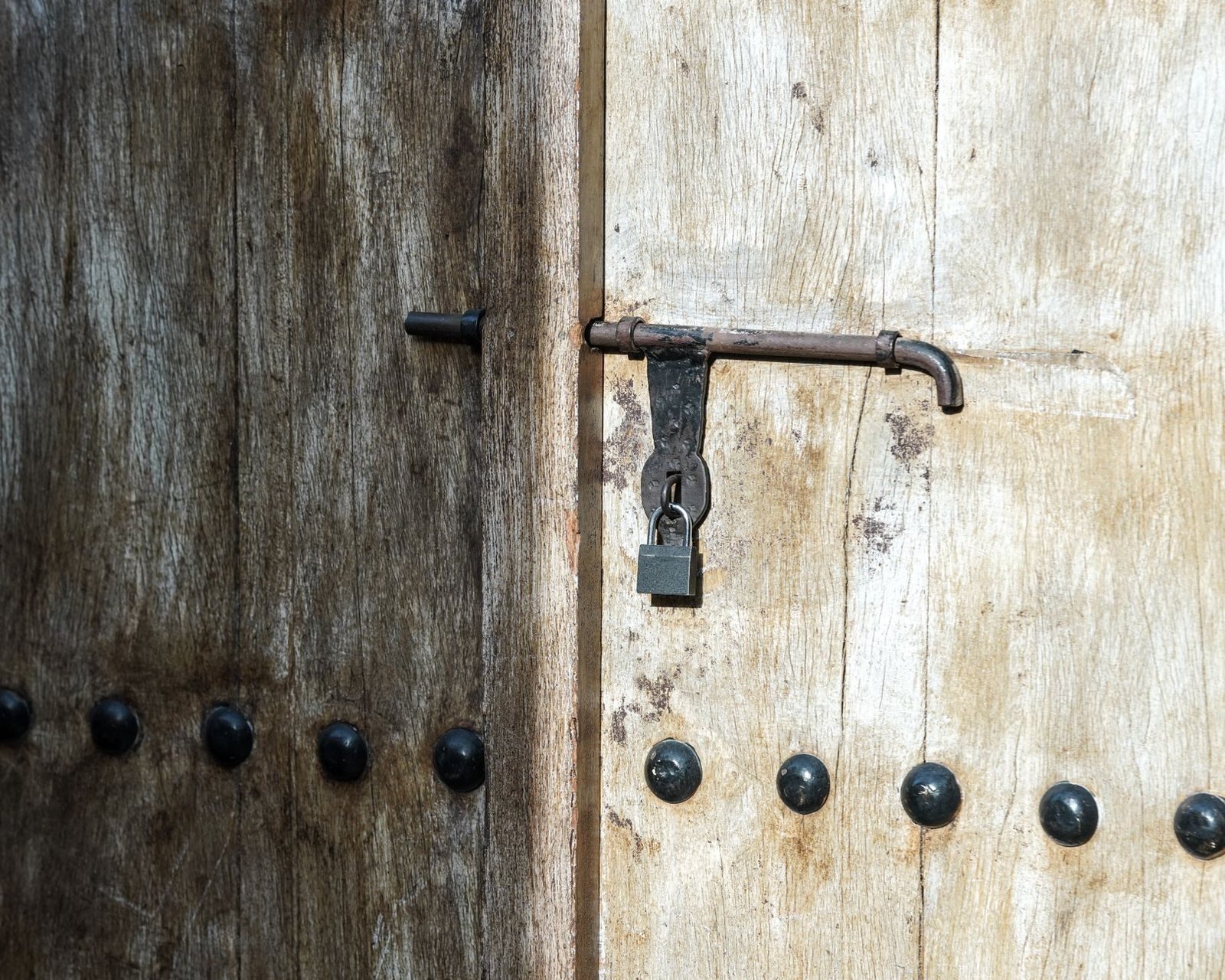 Close-up of a weathered wooden door with a vintage iron padlock in sunlight.