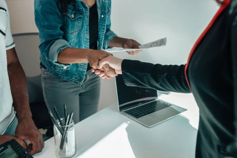Modalidades de licitação: como escolher o caminho certo da contratação 6 Two people shaking hands over a desk signifies a business agreement or partnership.
