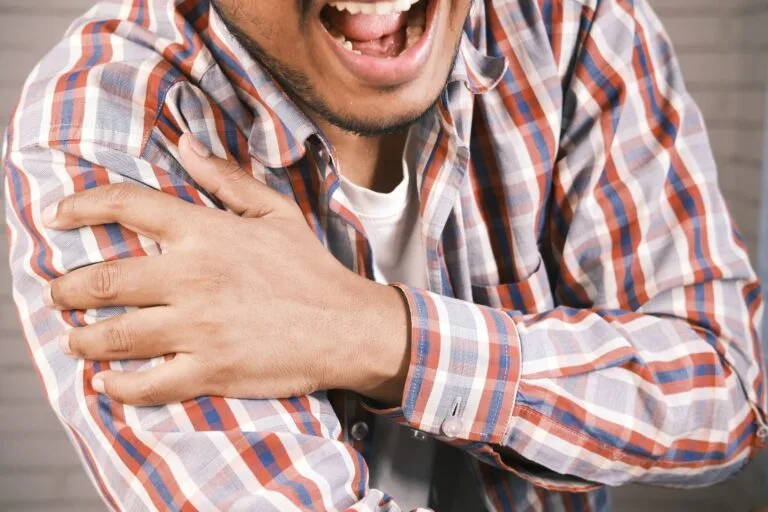 Close-up of a man in plaid shirt experiencing shoulder pain, grasping his arm.