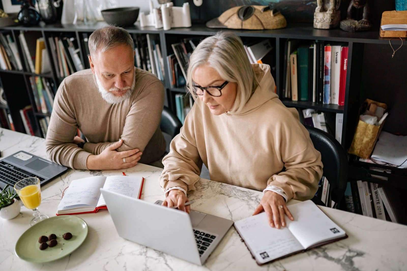 Pedagio de cinquenta por cento: para quem essa transicao realmente compensa 1 Elderly couple collaborating on laptops in a cozy home office setting.