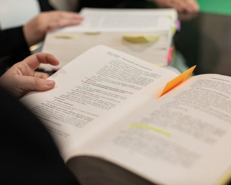 A close-up of hands holding books with highlighted text and notes, symbolizing learning and study.