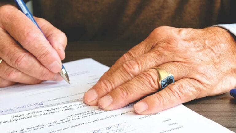 Perícia Médica INSS 2026: 10 Dicas Essenciais para Aprovação 2 Close-up of a senior adult signing a legal document with a focus on hand and gold ring.