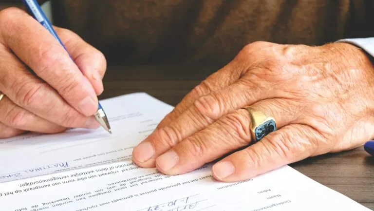 Perícia Médica INSS 2026: 10 Dicas Essenciais para Aprovação 2 Close-up of a senior adult signing a legal document with a focus on hand and gold ring.