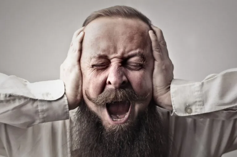 Perturbação do trabalho e do sossego: a contravenção que poucos conhecem 4 Portrait of a man with facial hair, covering his ears and screaming, expressing stress or frustration.