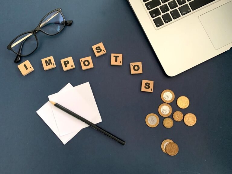 Top view of a workspace with coins, glasses, and the word impostos spelled out