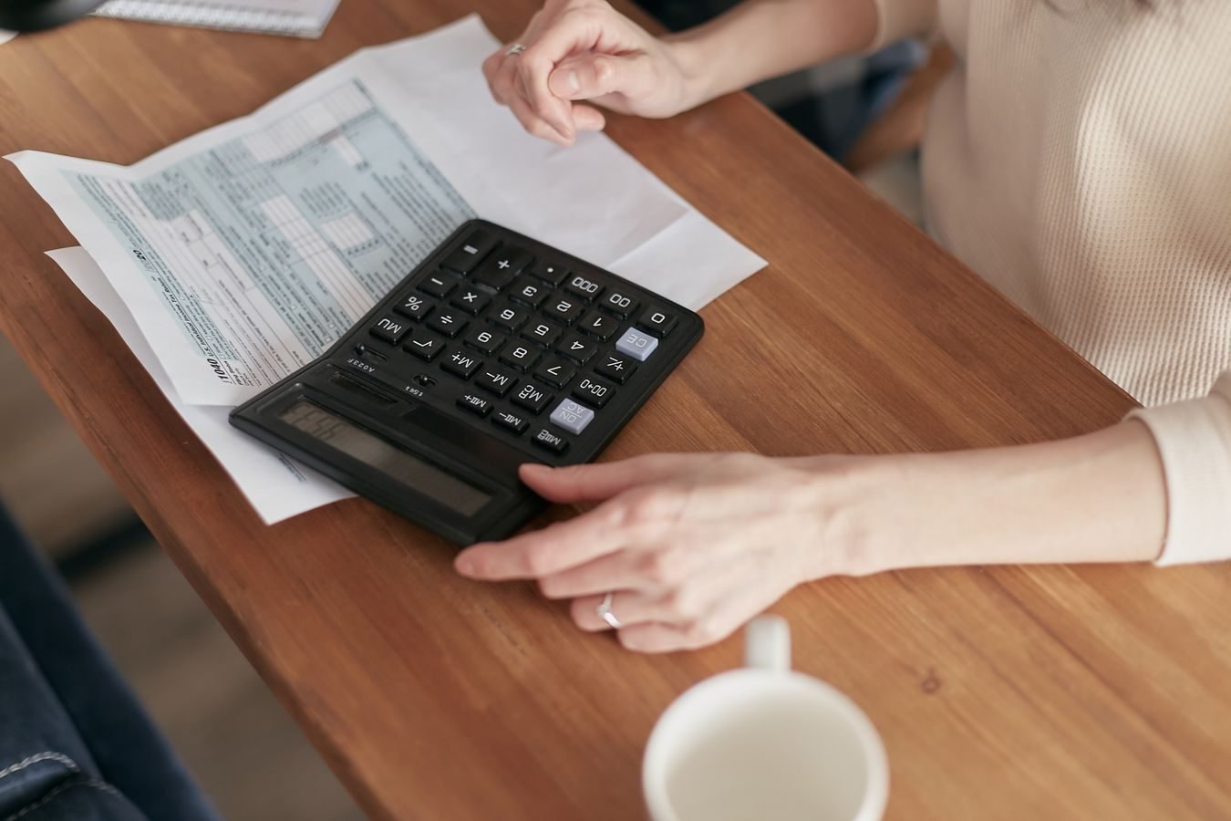 PIS e Cofins: entenda as contribuicoes e o aproveitamento de creditos 1 Focused individual using calculator to manage personal finances at wooden desk.