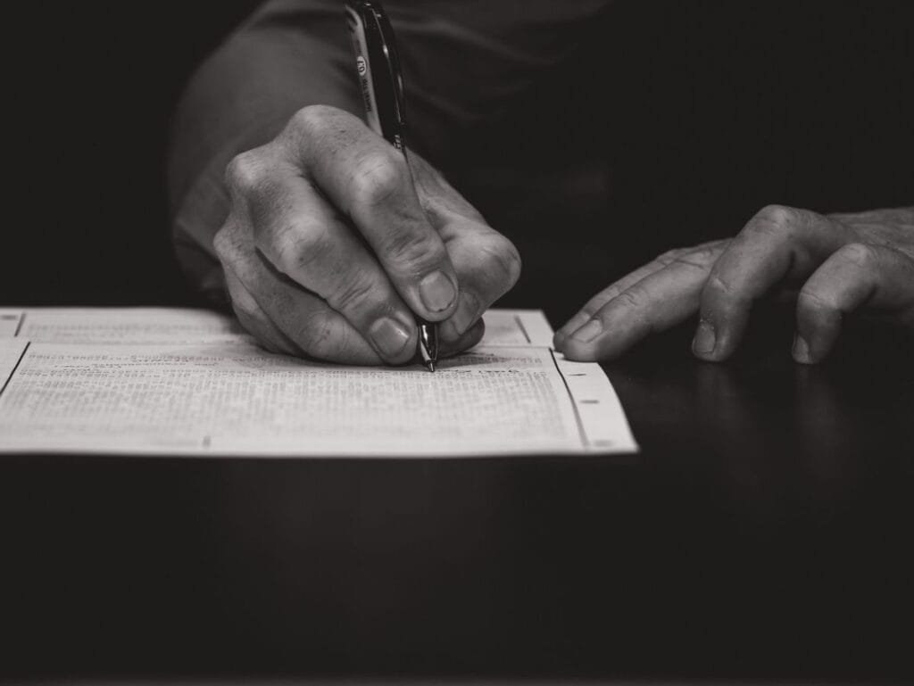 Quero me aposentar daqui a alguns anos. Vale a pena planejar antes? 1 Monochrome image of a hand writing on a document, emphasizing attention to detail.