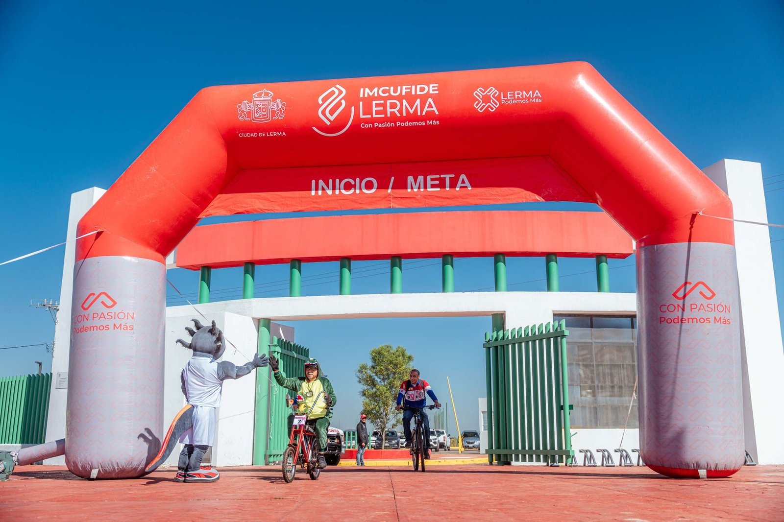 Cyclists start under the inflatable archway at a Lerma event with a dynamic mascot.