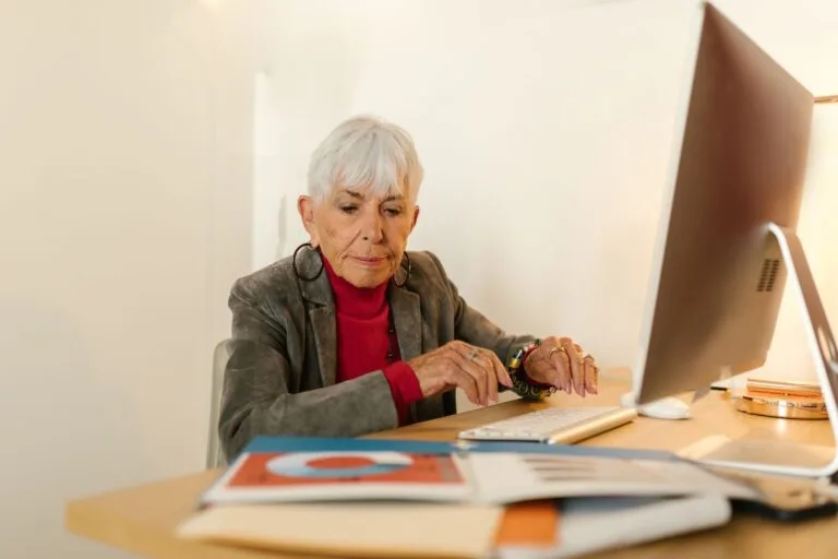Senior woman in business attire focusing on her work at a modern office desk.