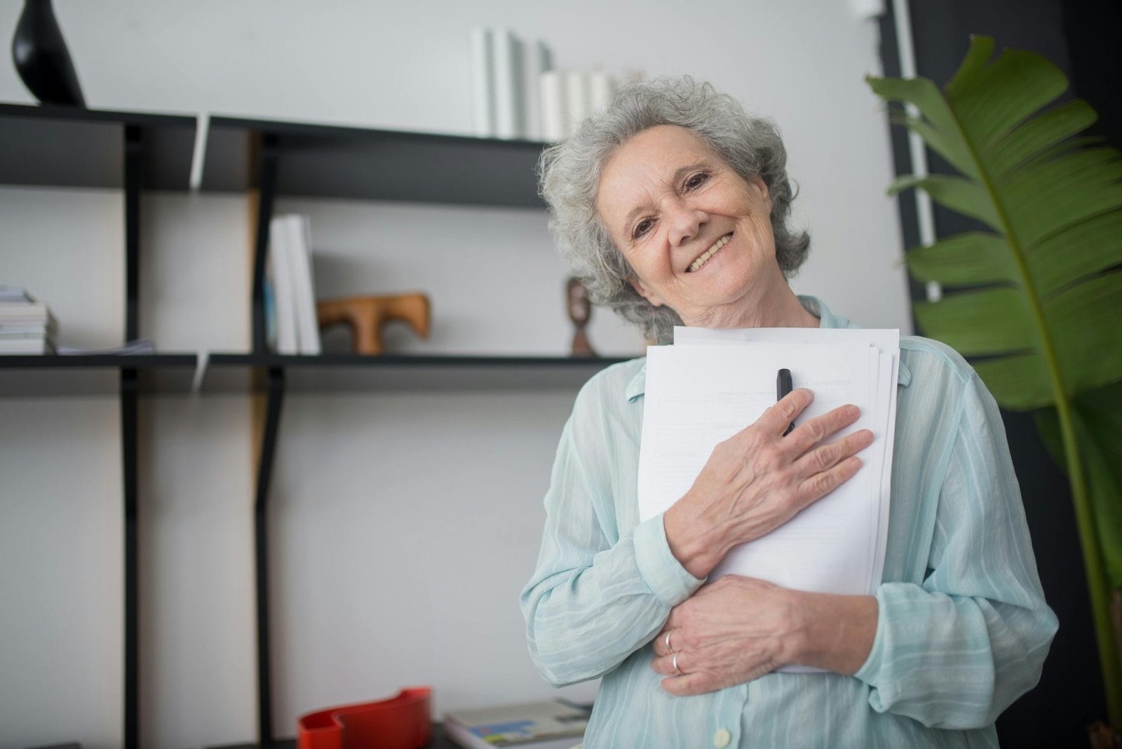 Senior woman smiling while holding papers indoors, showcasing happiness and contentment.